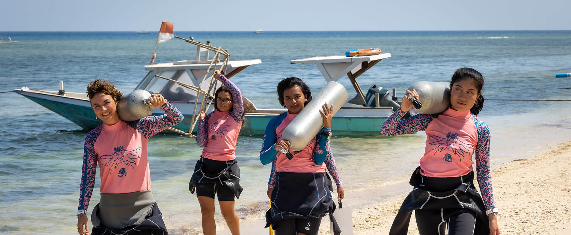 'Coral Catch' members in wetsuits carry oxygen tanks across beach