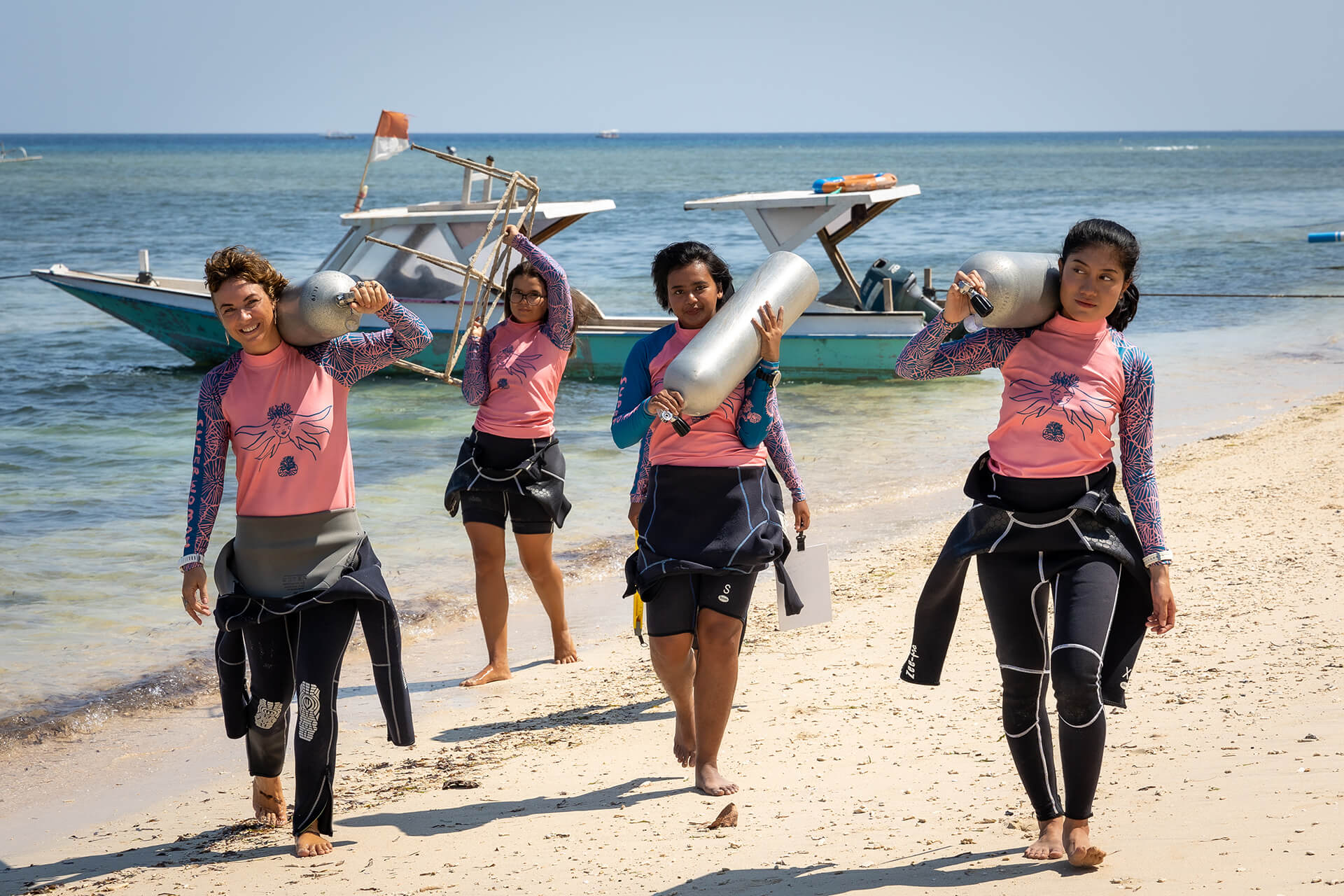 'Coral Catch' members in wetsuits carry oxygen tanks across beach