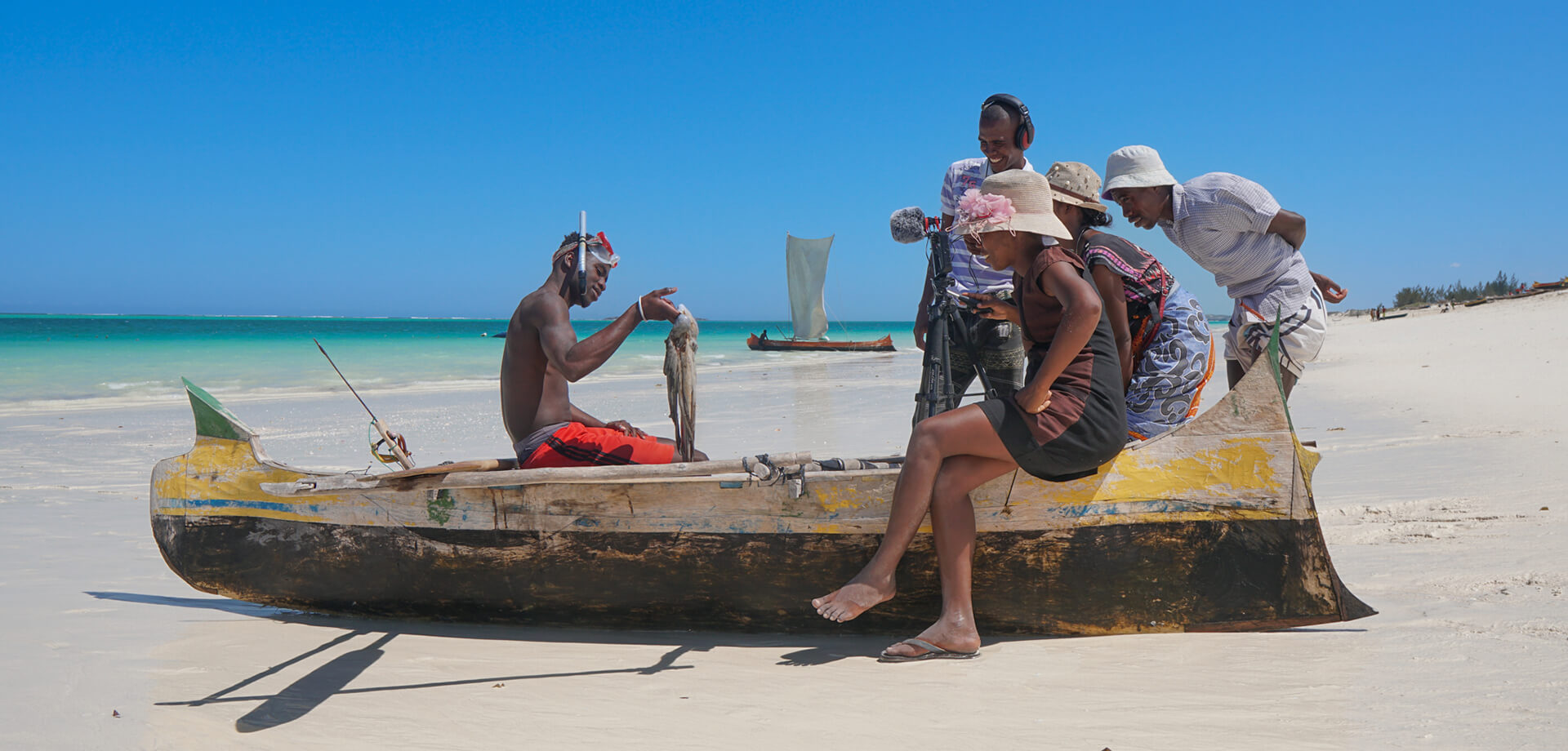 Group take video of fishing diver showing off his catch on tropical beach